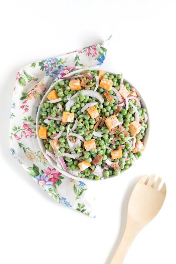 how to make classic pea salad, pea salad with bacon cheese chunks and slivered onions served in a white bowl with floral napkin and serving spoon nearby