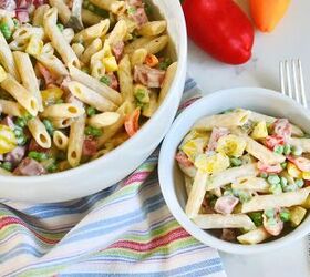 classic creamy german pasta salad nudelsalat, 2 white bowls with cream German pasta salad with fork on kitchen counter