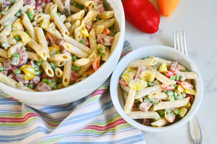 classic creamy german pasta salad nudelsalat, 2 white bowls with cream German pasta salad with fork on kitchen counter