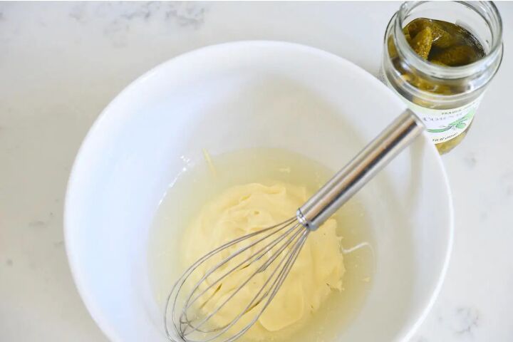 classic creamy german pasta salad nudelsalat, bowl with mayonnaise and pickle juice with wire whisk and jar of gherkins