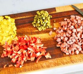 classic creamy german pasta salad nudelsalat, wooden chopping board with chopped yellow bell peppers red bell peppers cornichons and hot dogs