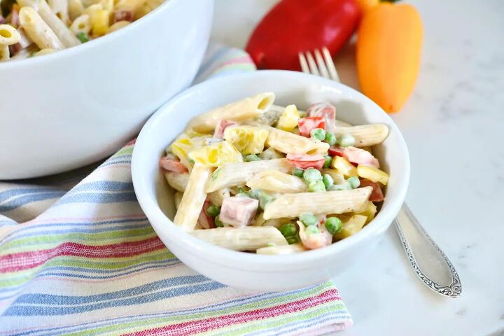 classic creamy german pasta salad nudelsalat, small bowl with classic German pasta salad on kitchen counter with fork bell peppers and tea towel