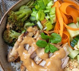 thai chicken rice bowls with peanut sauce, A close up of a Thai chicken rice bowl There s a peanut sauce drizzled on top The bowl has ribboned carrots diced cucumbers scallions and broccoli There s a sprig of fresh mint on top of the rice bowl
