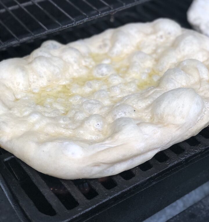 easy summer squash grilled pizza, Pizza dough that s been stretched into a rectangle shape and placed on the gas grill grates It s puffed up and you can see it s been rubbed with olive oil