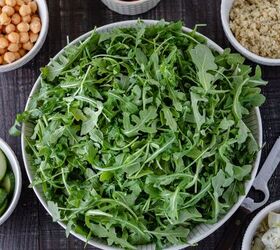 A large ceramic bowl filled with arugula and surrounded by small pinch bowls of sundried tomatoes garbanzo beans cucumber slices Kalamata olives artichoke hearts cooked quinoa and a homemade vinaigrette