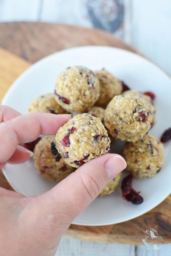 cranberry no bake energy bites recipe, Holding a cranberry energy bite with more on the plate below it