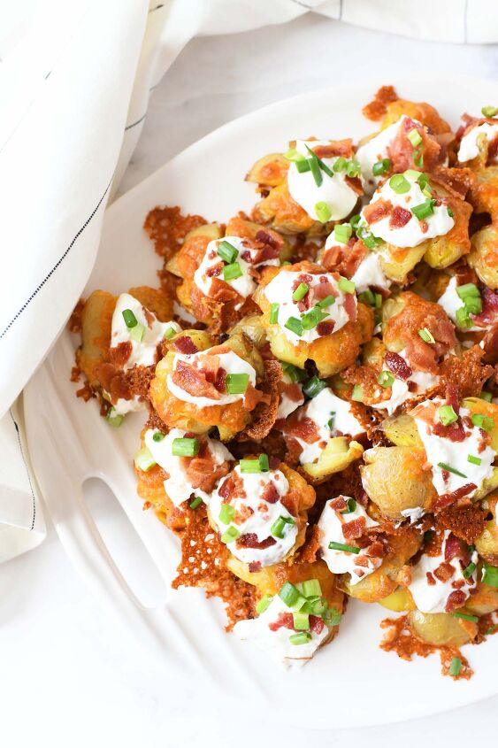 easy oven baked loaded smashed baby potatoes, Cheesy Smashed Potatoes on a white platter with a white napkin