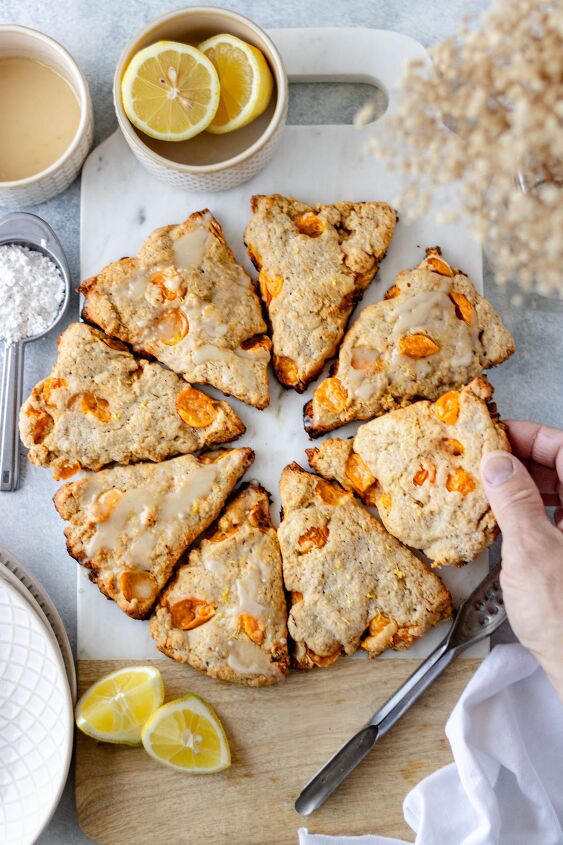 cape gooseberry scones with lemon, Eight scones arranged in a circle resting on a marble cutting board and a hand grabbing one scone