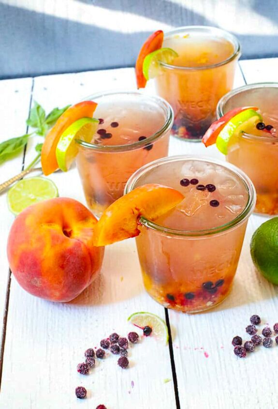 blueberry and peach vodka spritzer, glassed with ice and frozen blueberries and slices of lime and peaches