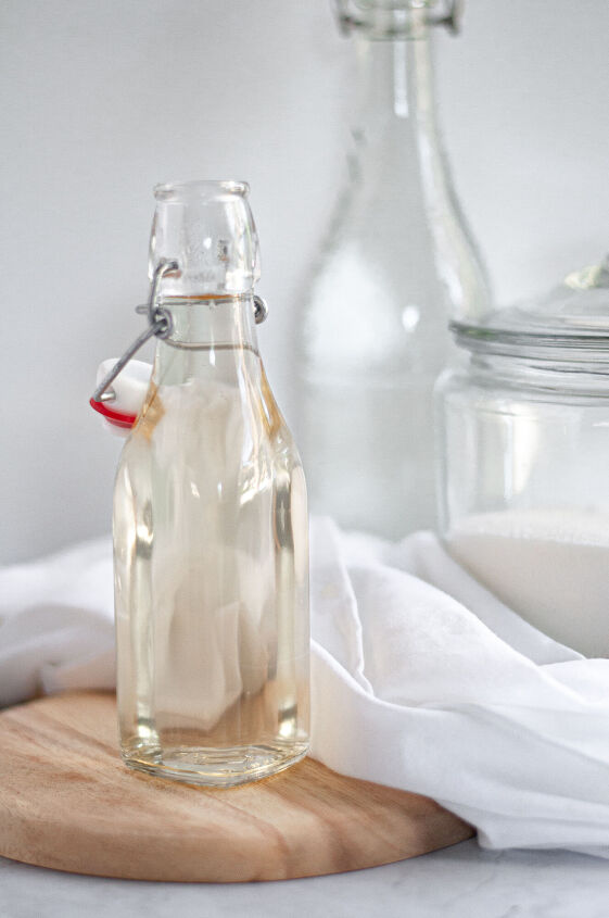 simple syrup, Container of simple syrup on a wooden block with a napkin jug of water and container of sugar in the background