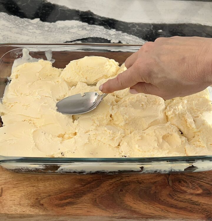 easy homemade buster bar ice cream dessert recipe, Using the back of a spoon to spread a layer of vanilla ice cream over the cookie crust
