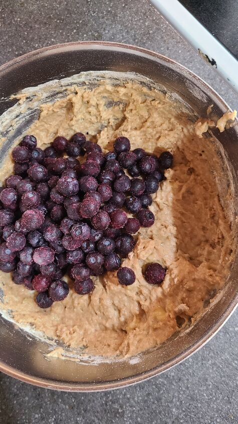 the best banana blueberry muffins recipe, A bowl full of muffin mix topped with frozen blueberries