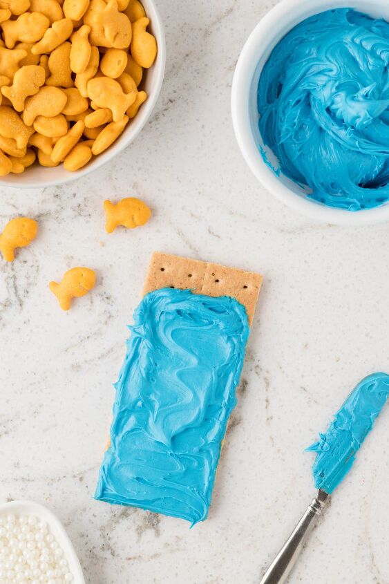 make ocean themed graham cracker snacks for a fun day, spreading blue frosting onto a graham cracker