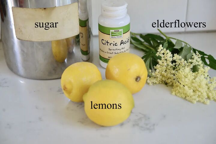 simple homemade elderflower syrup recipe, jar of sugar bottle of citric acid elderflowers and 3 lemons on kitchen counter