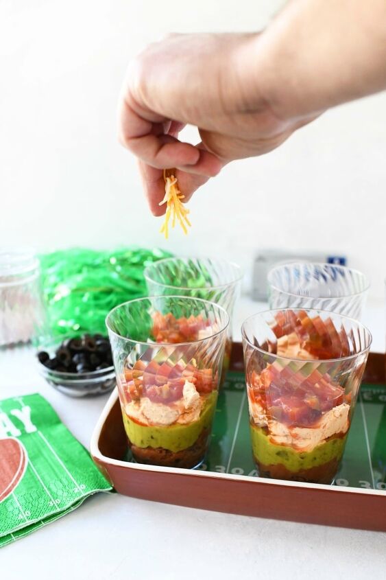 7 layer game day individual dip cups, 7 layer dip cups being made with a hand sprinkling cheese