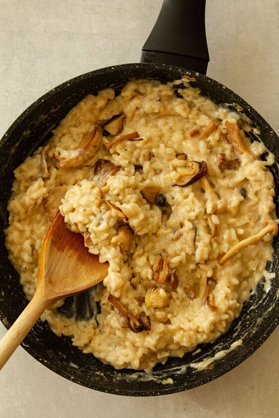 risotto ai funghi mushroom garlic and parmesan risotto, Stirring in in the Parmesan cream balsamic vinegar and mushrooms with a wooden spoon in a dark coloured frying pan