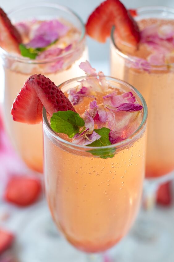 sparkling strawberry rose cocktail, 3 champagne flutes filled with sparkling ros They re topped with edible rose petals and a slice of fresh strawberry