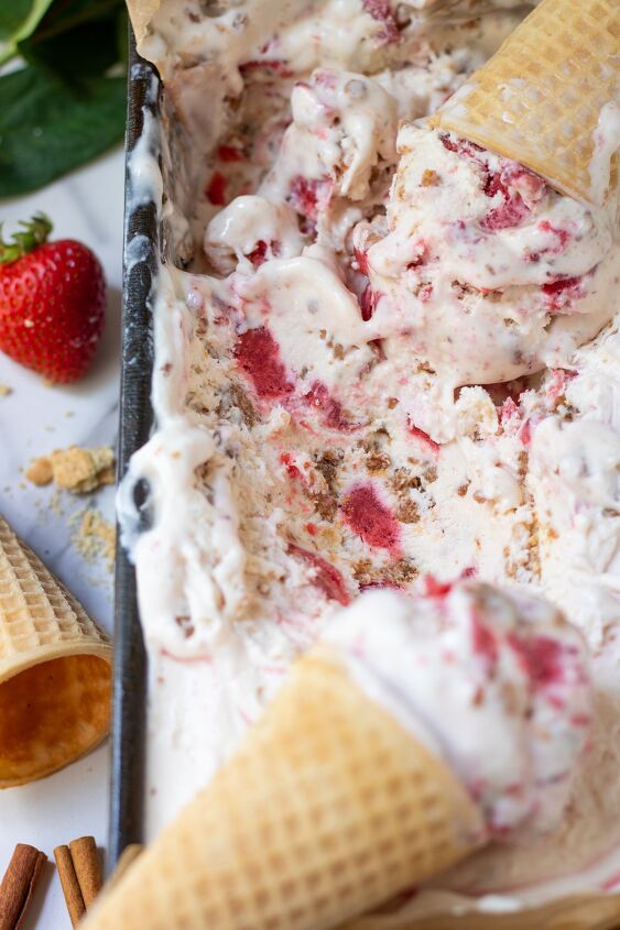 A metal loaf pan filled with no churn strawberry crumble ice cream There s an ice cream cone on top You can see pieces of crumble and strawberries in the ice cream