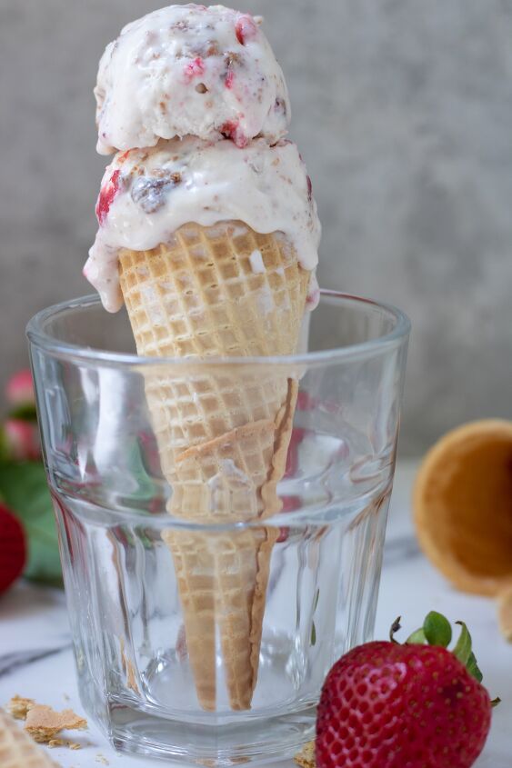 A short glass with an ice cream cone in it There s ice cream dripping down the sides you can see more ice cream cones and a strawberry in the background