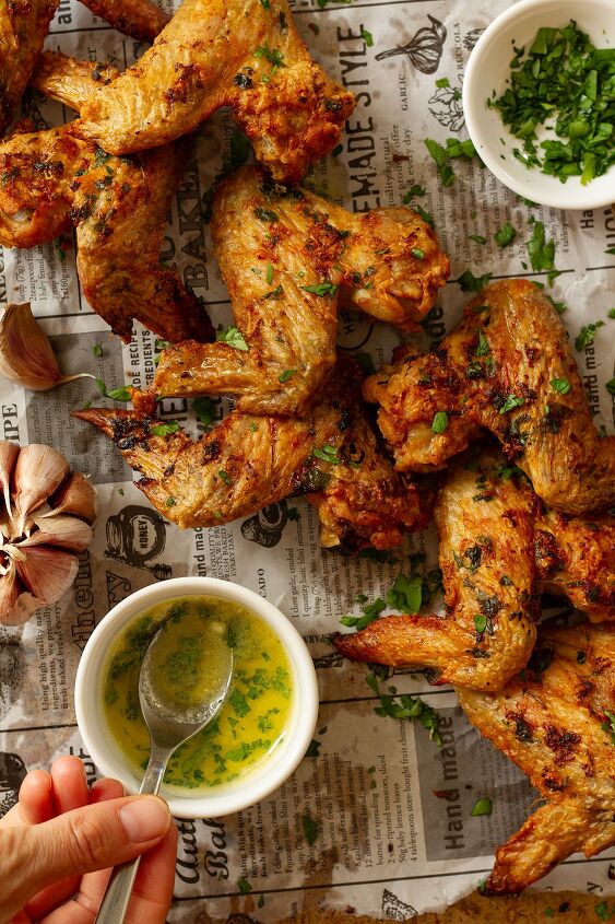 garlic butter chicken wings oven baked and super crispy, Garlic Butter Wings served topped with parsley and side dishes of parsley and melted butter and garlic sauce on a newspaper themed background