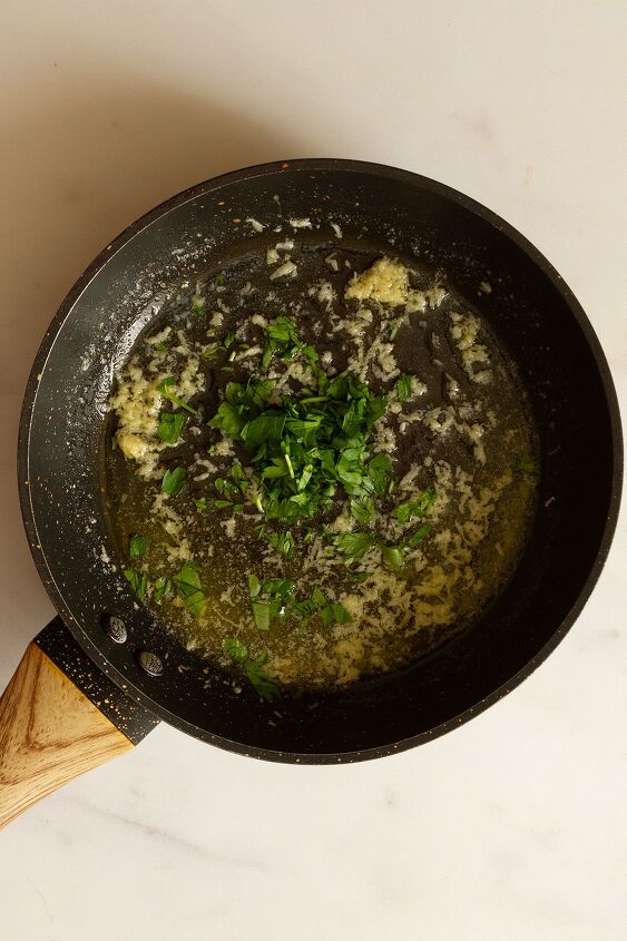 garlic butter chicken wings oven baked and super crispy, Preparing the melted butter and garlic sauce with added parsley in a dark coloured saucepan