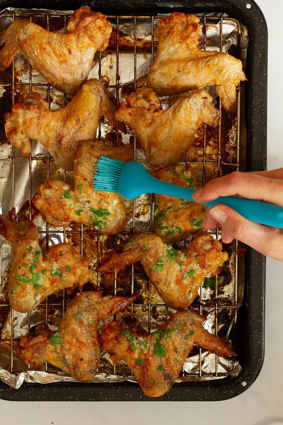 garlic butter chicken wings oven baked and super crispy, Brushing the cooked chicken wings with the garlic butter sauce using a blue silicone brush