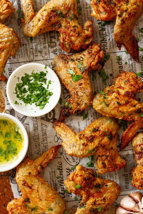 garlic butter chicken wings oven baked and super crispy, Garlic Butter Wings served topped with parsley and side dishes of parsley and melted butter and garlic sauce on a newspaper themed background