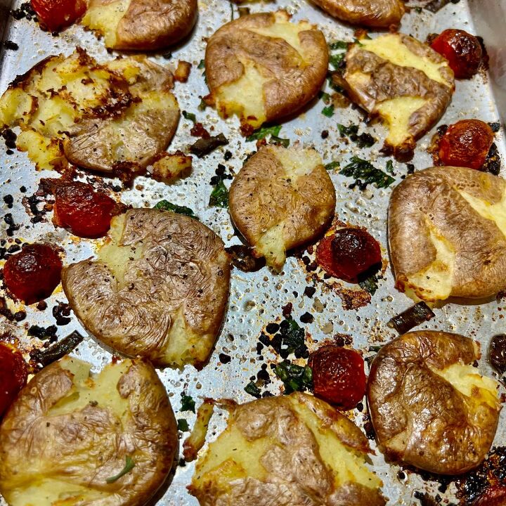 the crispiest air fryer smashed potatoes, Air fryer smashed potatoes on a baking sheet pan with cherry tomatoes and herbs