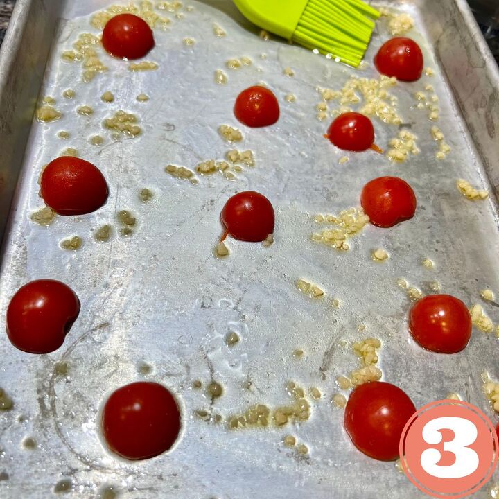the crispiest air fryer smashed potatoes, sheet pan with grape tomatoes olive oil and crushed garlic being mixed with a green brush