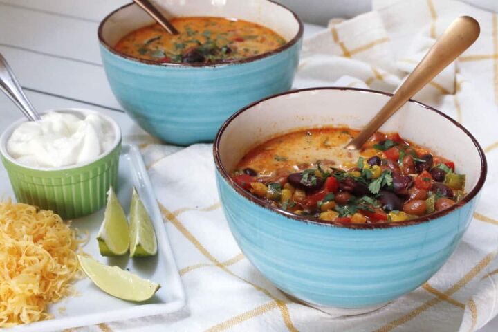 creamy mexican bean soup with corn, Two blue bowl of Mexican corn and bean soup with a plate of cheese limes and sour cream