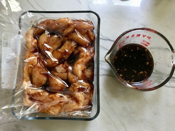 chinese chicken on a stick recipe garlic sesame sauce, Raw chicken marinating in a storage bag in a glass container on counter with extra marinade in a measuring cup to the side for Chinese Chicken on a Stick Recipe