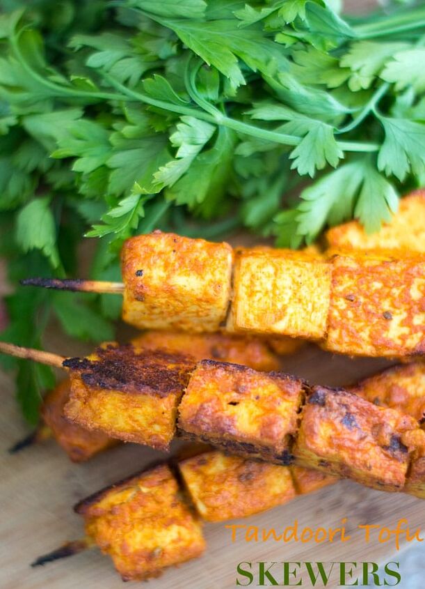 tandoori tofu skewers recipe, Overhead and Closeup View of Skewered Tofu Oven Roasted and Stacked on each other Two Skewers with 3 Tandoori Tofu Squares Each are Placed at the Bottom of the Stack and on Top of a Brown Board Two Other Skewers With four 1 Tofu Squares are Stacked on Top Diagonally A Bunch of Italian Parsley is Placed Behind the Skewers
