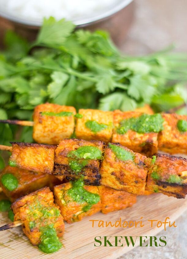 tandoori tofu skewers recipe, Front and Closeup View of Skewered Tofu Oven Roasted and Stacked on each other Two Skewers with 3 Tandoori Tofu Squares Each are Placed at the Bottom of the Stack and on Top of a Brown Board Two Other Skewers With four 1 Tofu Squares are Stacked on Top Diagonally Green Chutney is Lightly Drizzled Over the Tofu A Bunch of Italian Parsley is Placed Behind the Skewers