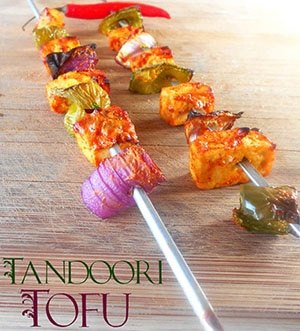 tandoori tofu skewers recipe, Front View of 2 Skewers Filled with Grilled Tofu Bell Pepper Onions and On Red Chili Pepper The Skewers are Arranged Diagonally on a Brown Board