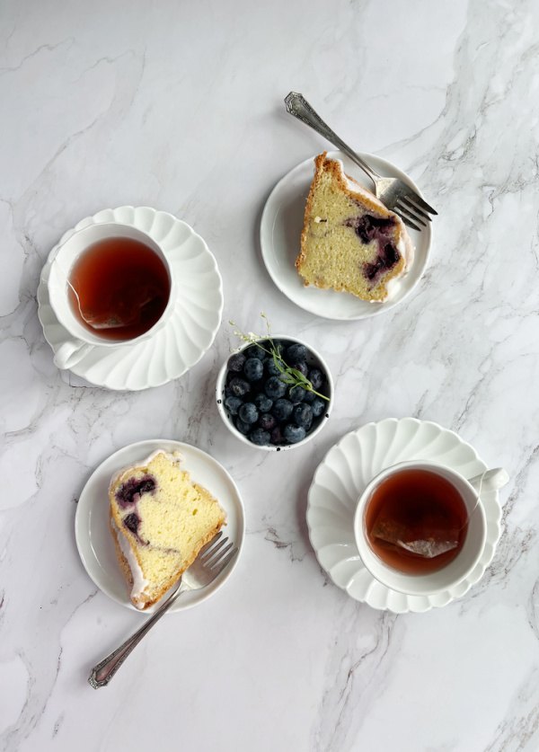 bonne maman blueberry swirl bundt cake, blueberry swirl bundt cake on 2 plates with 2 cups of tea and a bowl of blueberries