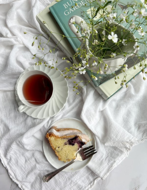 bonne maman blueberry swirl bundt cake, Blueberry Swirl Bundt Cake on a plate with a cup of tea and a pile of books with white flowers