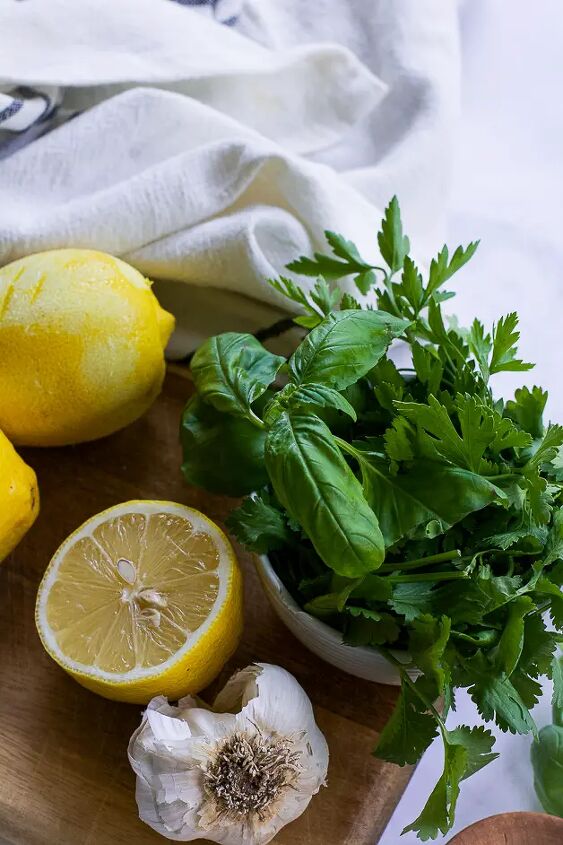 mediterranean herbed tahini sauce, fresh herbs on a cutting board with a zested lemon a lemon half and a head of garlic