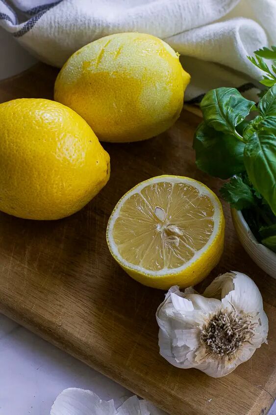 mediterranean herbed tahini sauce, lemons a garlic head and fresh herbs on a cutting board
