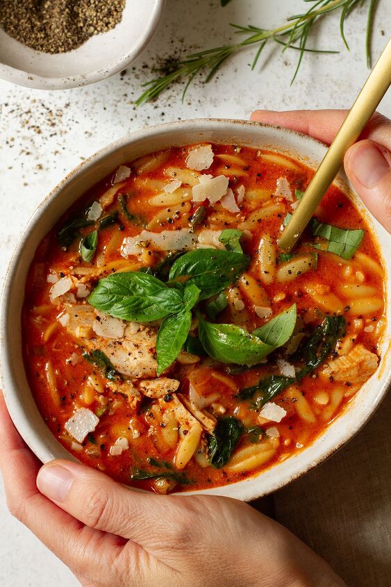 rosa mariana soup italian orzo soup with chicken and tomato, A hand held serving of Rosa Marina Soup with basil in a cream coloured bowl with Parmesan Rosemary and pepper on the side