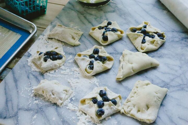 easy blueberry puff pastry turnovers, raw pastry dough filled with blueberries on a marble backdrop