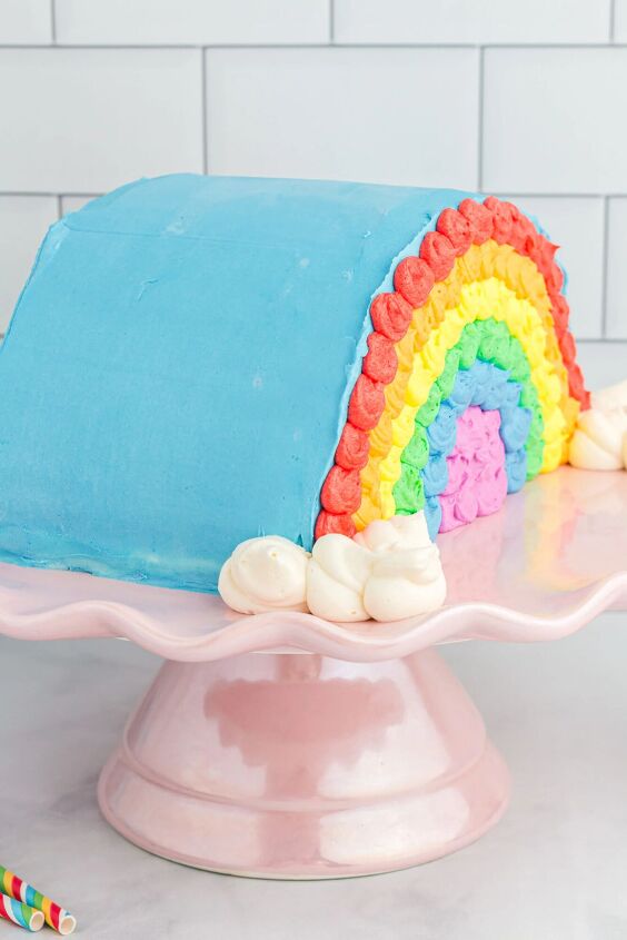 how to make a funfetti rainbow cake perfect for every celebration, side view of pretty rainbow decorated cake on a pink cake stand