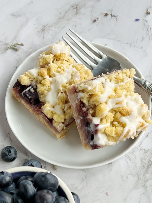 blueberry crumb bars, blueberry crumb bars stacked in a plate with a fork and a small bowl of blueberries