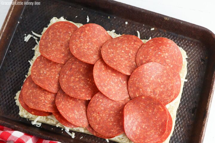 pepperoni pizza sliders, Bottom slab of rolls sitting on a baking sheet sprinkled with mozzarella cheese and a layer of pepperoni slices