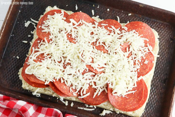 pepperoni pizza sliders, Bottom slab of rolls sitting on a baking sheet sprinkled with mozzarella cheese a layer of pepperoni slices and topped with more mozzarella cheese