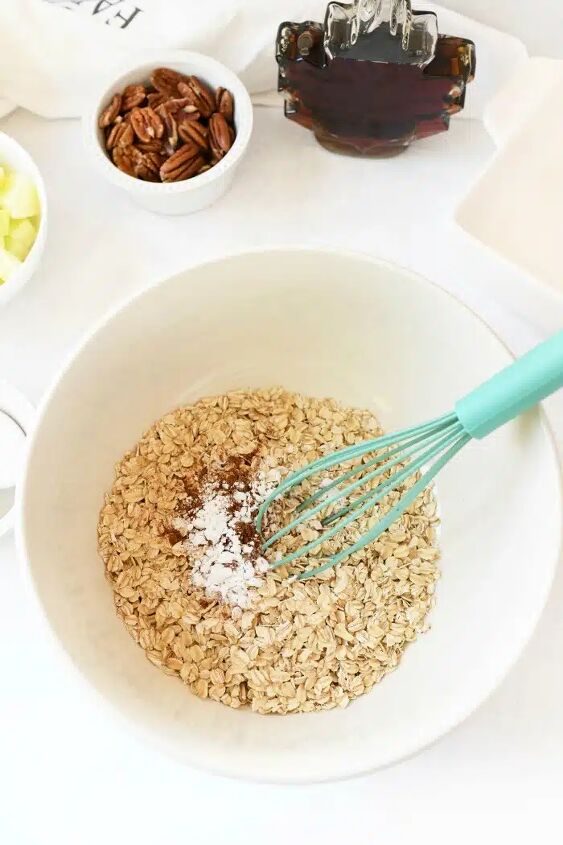 baked apple oatmeal, oatmeal ingredients in a large bowl with a blue whisk