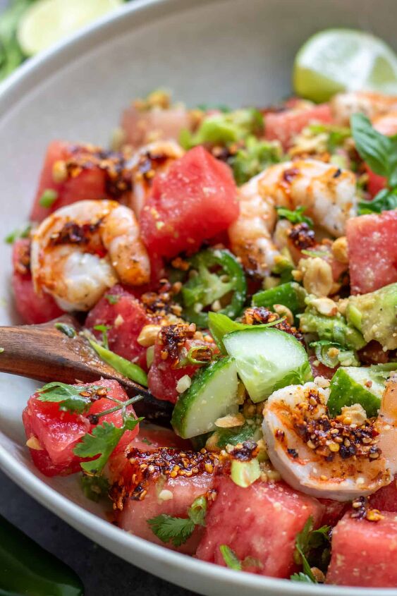 spicy watermelon salad with shrimp, Watermelon salad with diced cucumbers avocado and sliced jalape o peppers There s a wooden serving spoon in the salad bowl It s drizzled with a chili crunch oil and topped with grilled shrimp