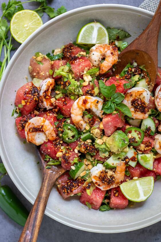 spicy watermelon salad with shrimp, A large round salad bowl filled with spicy watermelon salad topped with grilled shrimp There s a fresh sprig of mint in the middle and the salad is drizzled with chili crunch oil You can see the diced cucumbers and avocado Two serving spoons are in the salad bowl