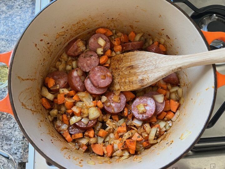 galinhada dutch oven chicken and rice, Cooked sausage slices added to Carrots onions and garlic cooking in a pot for Galinhada Dutch Oven Chicken and Rice