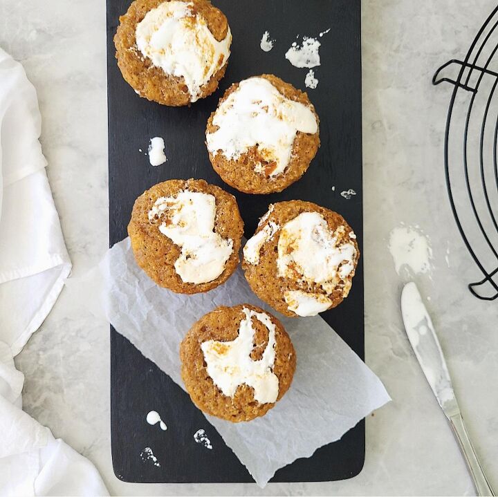 marshmallow swirl sweet potato muffins, sweet potato muffins with marshmallow fluff on top top down view of 5 muffins staggered on a black cutting board there are dips of white marshmallow contrasting on the black wood background is gray marble