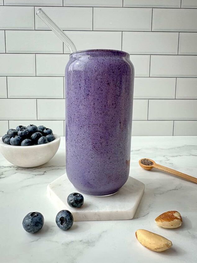 blueberry protein shake, Blueberry protein shake in a clear glass with a straw Blueberries chia seeds and nuts surround the glass
